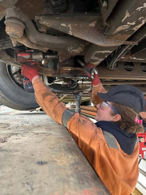 A mechanic working underneath a truck with a power tool