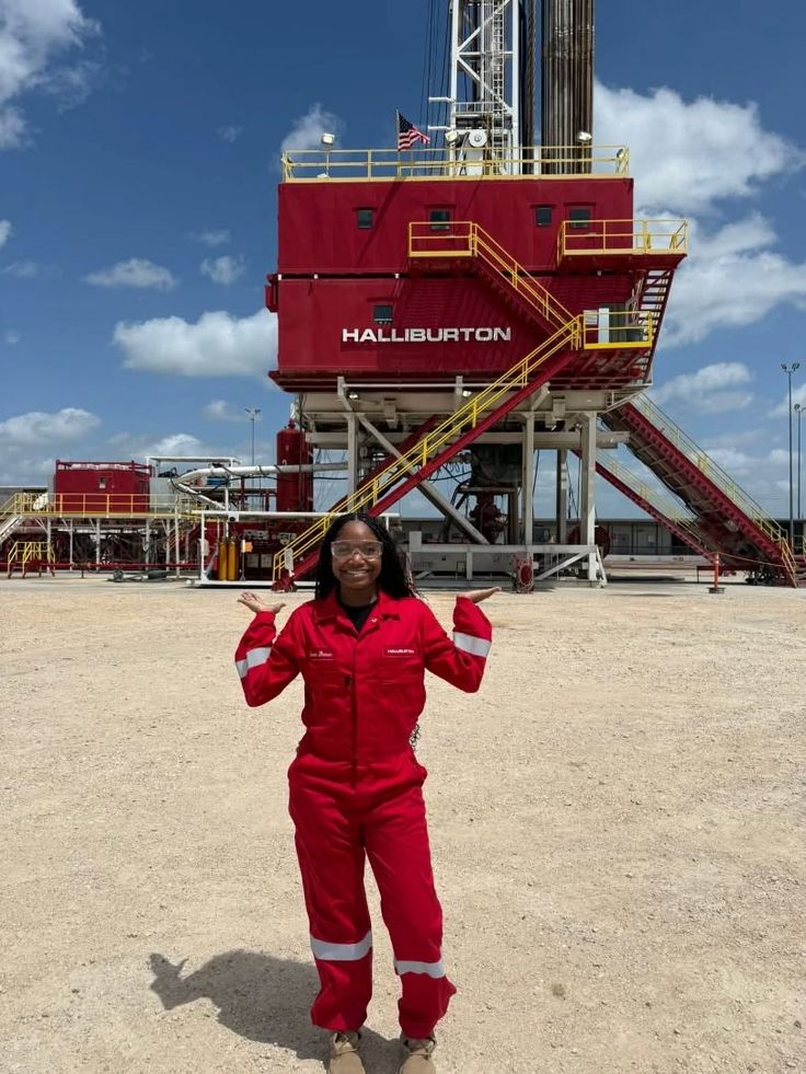 An oilfield worker in coveralls in front of a drilling rig