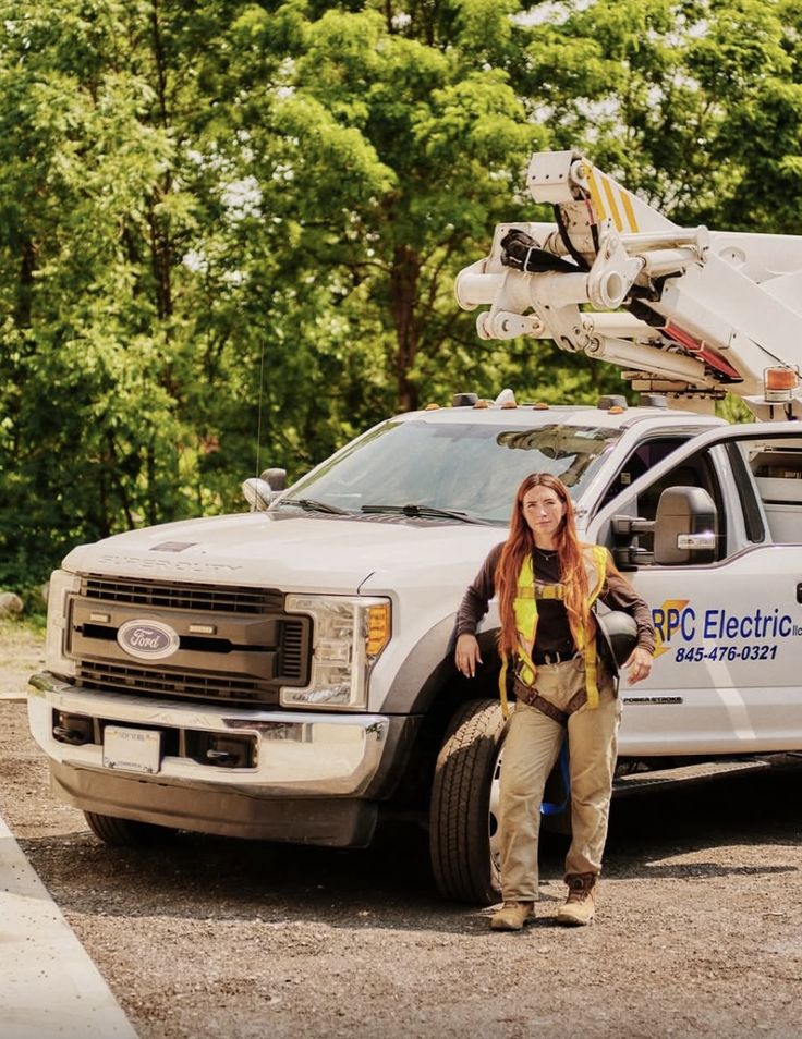 An electrical lineworker standing beside her bucket truck