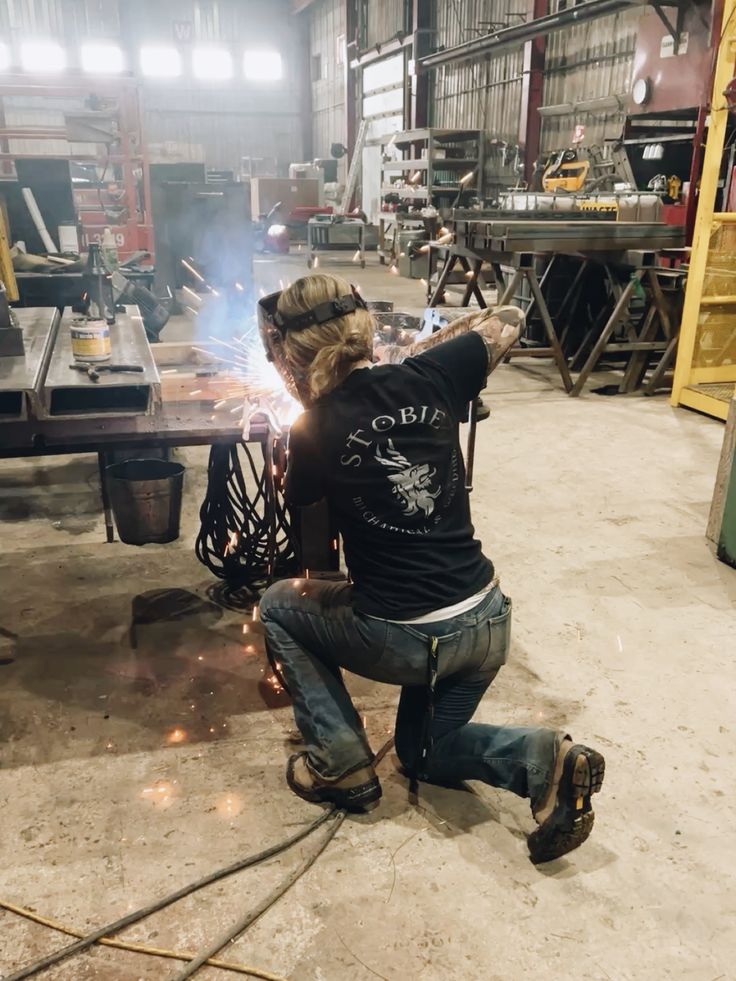 A tradeswoman welding, sparks flying in a fabrication shop